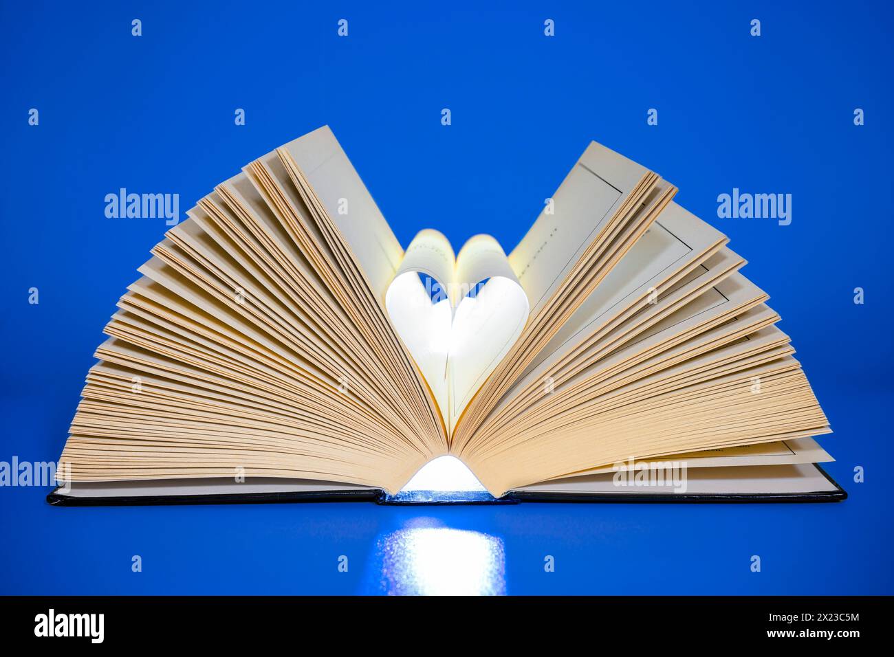 Öffnen Sie das Buch auf blauem Hintergrund mit den mittleren Seiten in Herzform Stockfoto