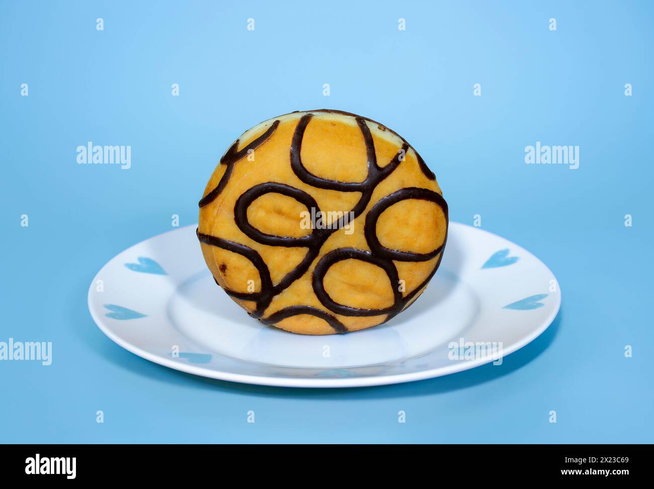 Mit Schokolade gefüllter Donut stehend auf einem hübschen blau-weißen Teller, auf blauem Hintergrund Stockfoto