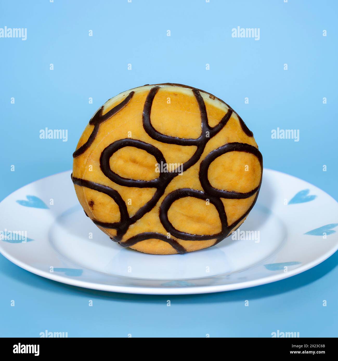 Mit Schokolade gefüllter Donut stehend auf einem hübschen blau-weißen Teller, auf blauem Hintergrund Stockfoto