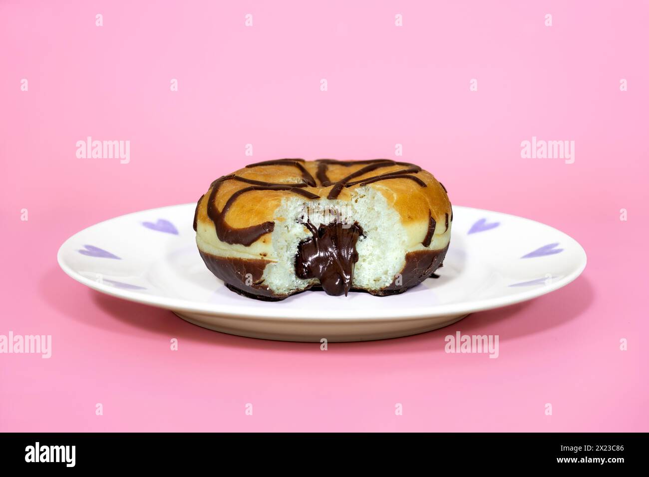 Mit Schokolade gefüllter Donut mit herausgenommenem Biss, und sprudelnder Schokoladenfüllung, auf rosa Hintergrund und hübschem Teller Stockfoto