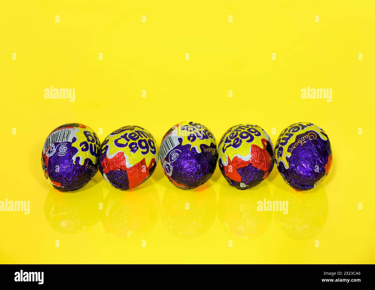 Fünf Cadbury Creme Eier hintereinander auf gelbem Hintergrund, Ostereier Stockfoto