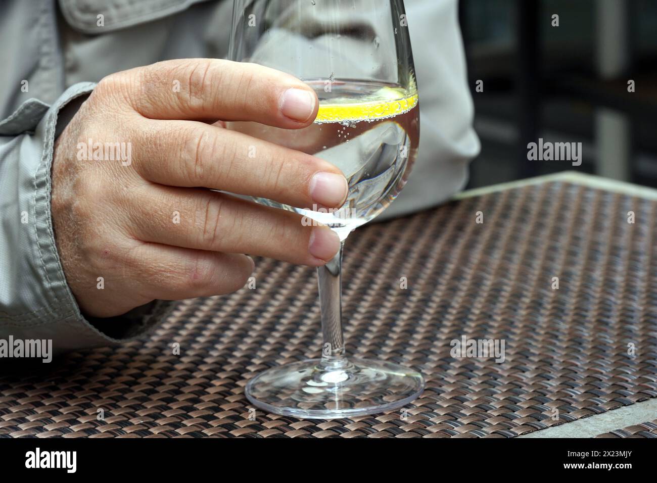 Eine männliche Hand hält ein Weinglas mit Wasser und eine Scheibe Zitrone im Café draußen. Stockfoto