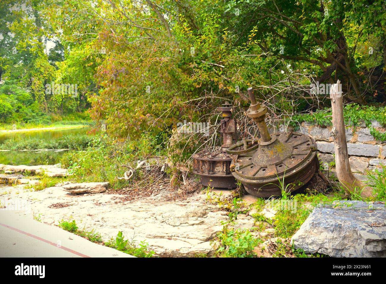 Große, rostige Teile, wahrscheinlich aus der alten Mühle, befinden sich in der Nähe eines alten Fundaments neben dem Big Sugar Creek in der Nähe von Pineville, MO, Missouri, USA. Stockfoto