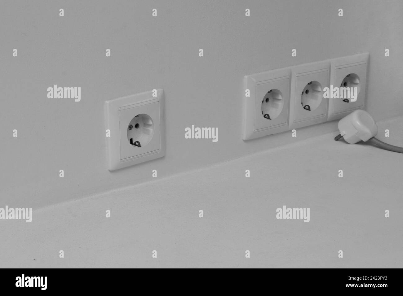 Steckdose an einem grauen Kopierraum an der Wand. Ein weißer Stecker, der nicht in eine Steckdose gesteckt ist. Stockfoto