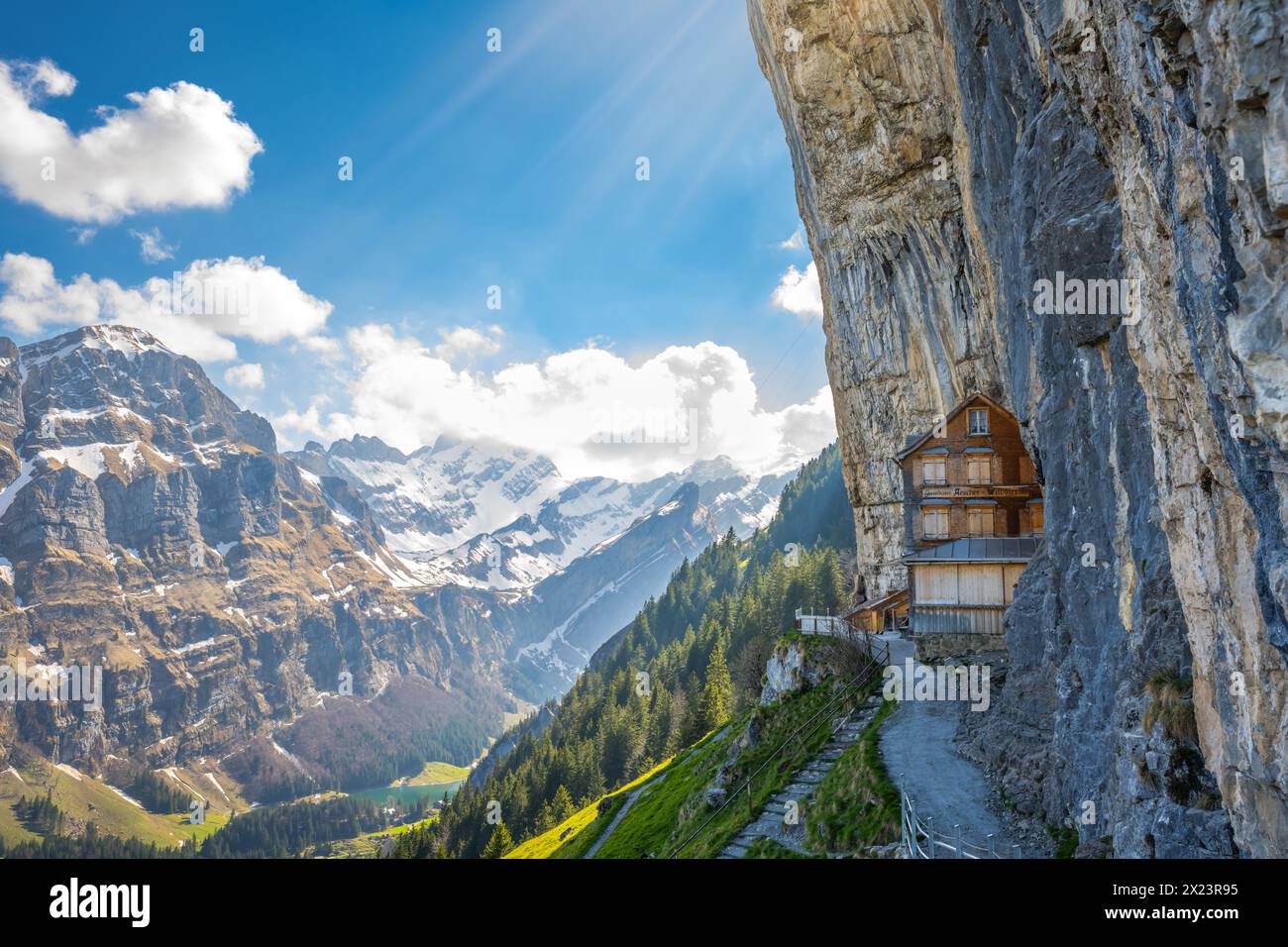 Beschreibung: schweizer Holzhütte Gasthaus Aescher-Wildkirchli unter massiver überhängender Felsmauer und malerischer Bergkette im Hintergrund. Seealp Stockfoto