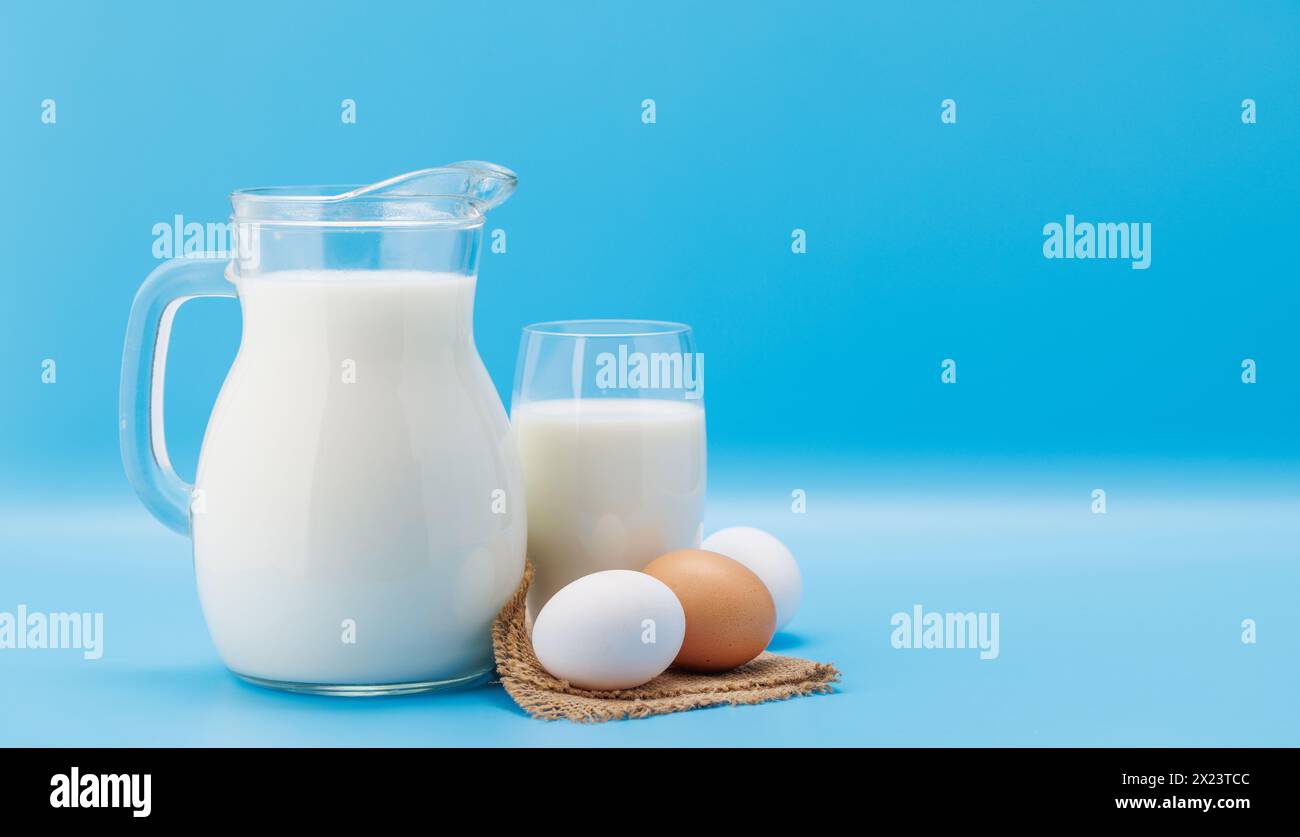 Milchkrug mit Eiern auf blauem Hintergrund mit Kopierraum Stockfoto