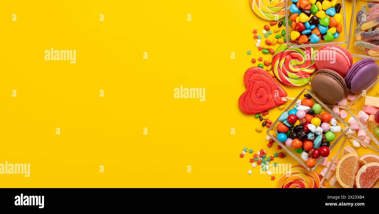 Verschiedene bunte Süßigkeiten, Lutscher und Makronen. Flache Süßigkeiten auf gelbem Hintergrund mit Kopierraum Stockfoto