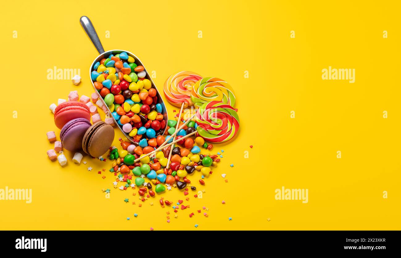 Verschiedene bunte Süßigkeiten, Lutscher und Makronen. Über gelbem Hintergrund mit Kopierraum Stockfoto