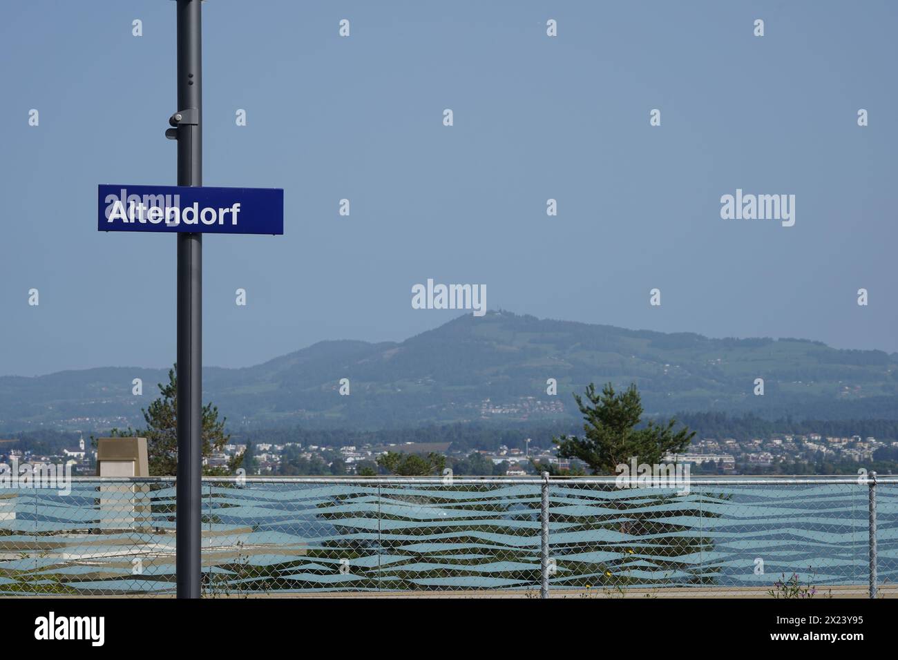 Metallschild mit blauem Schild, das den Namen des Dorfes Altendorf in der Schweiz sagt. Der Zürichsee und die Berge liegen im Hintergrund. Stockfoto