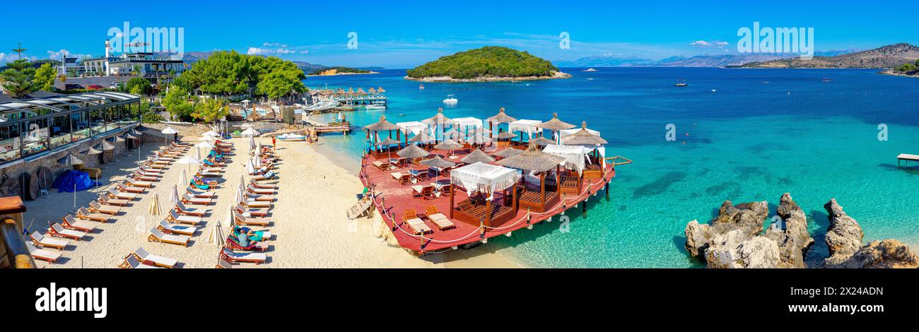 Freizeitplattform unter kristallklarem Wasser mit einer Insel im Hintergrund des paradiesischen Strandes von Ksamil-Albanien. Stockfoto