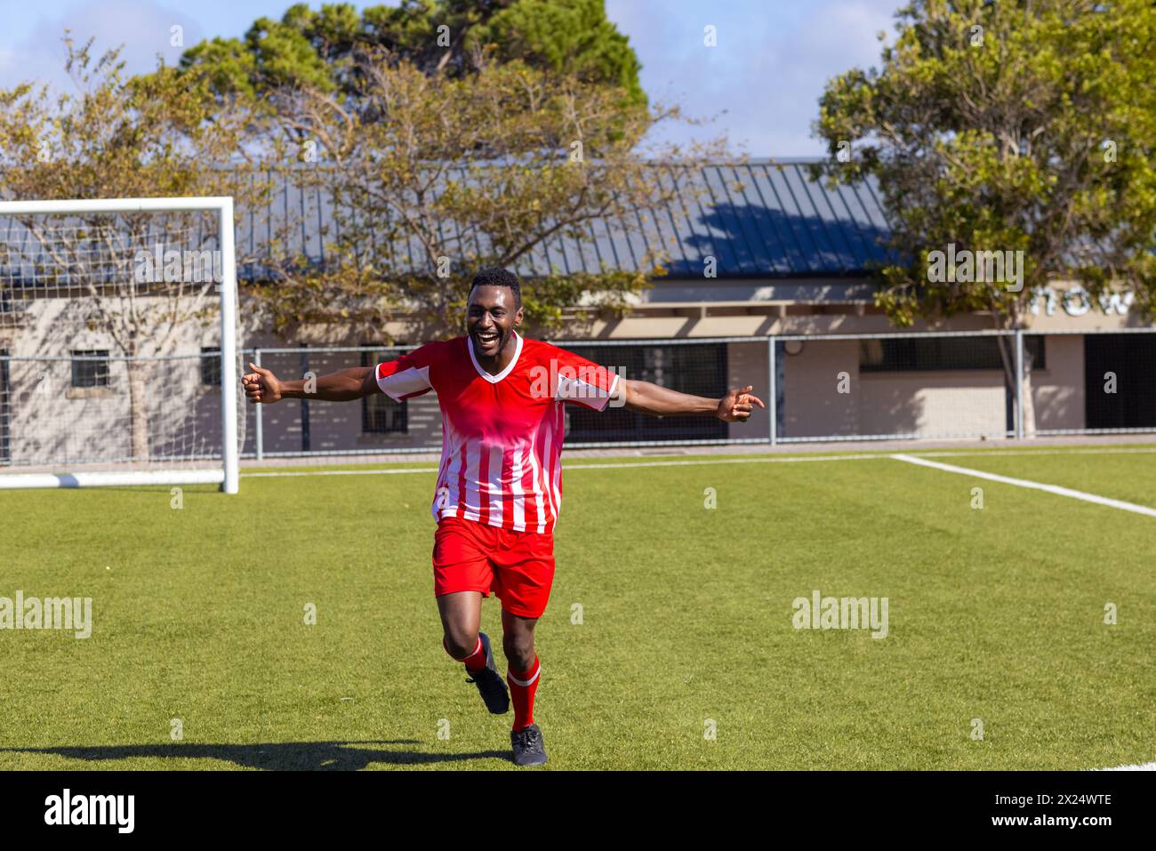 Afroamerikanischer junger männlicher Athlet in rot-weißer Fußballuniform, der draußen auf dem Feld läuft Stockfoto