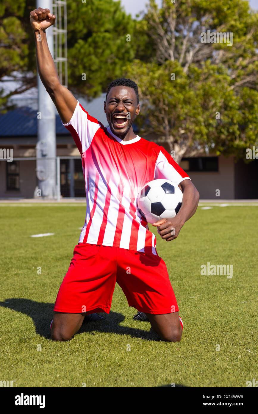 Ein afroamerikanischer junger männlicher Athlet, der draußen auf dem Fußballfeld feiert und einen Ball hält Stockfoto