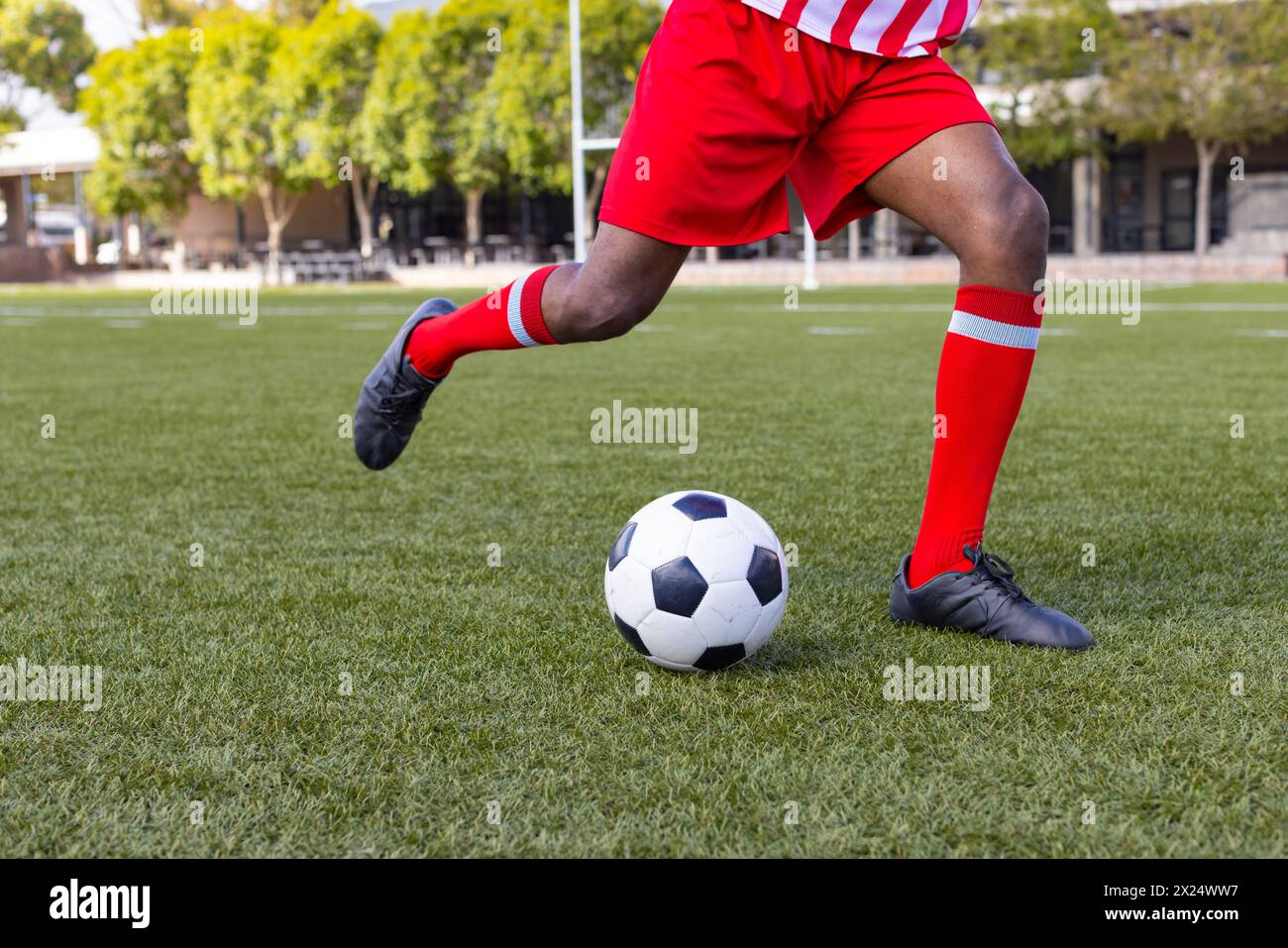 Afroamerikaner in roter, weißer Ausrüstung tritt einen Fußball Stockfoto