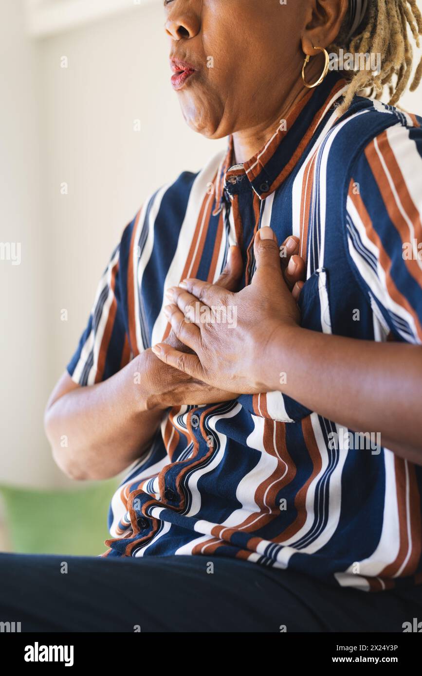 Eine ältere Afroamerikanerin mit goldenen Ohrringen hält ihre Brust zu Hause Stockfoto