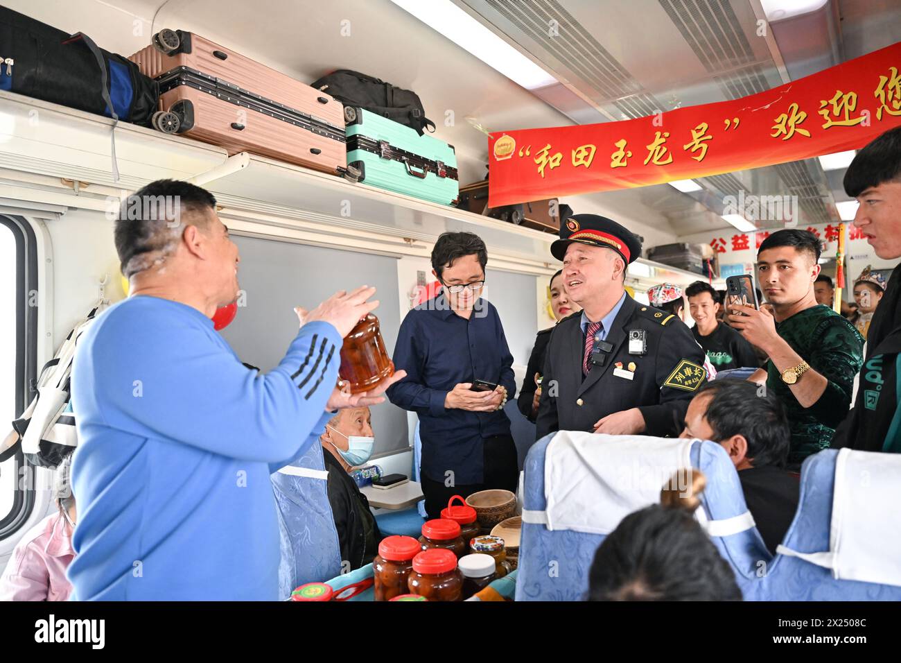 (240420) -- URUMQI, 20. April 2024 (Xinhua) -- Yimamamat Saipar (1. L), ein Verkäufer aus Atux in der nordwestchinesischen Autonomen Region Xinjiang Uygur, wirbt Feigenprodukte an Bord des Zuges Nr. 7556, 3. April 2024. Der gemächliche grüne Zug Nr. 7556 verbindet Urumqi, die Hauptstadt der Autonomen Region Xinjiang Uygur im Nordwesten Chinas, mit Hotan im südlichen Ausläufer der Region und fährt mit einer Geschwindigkeit von unter 80 km pro Stunde. In den letzten 13 Jahren seit seiner Inbetriebnahme diente dieser langsame Zug jedoch als Marktplatz für mehr als 15 Millionen Passagiere während seiner 31-stündigen Fahrt. Stockfoto