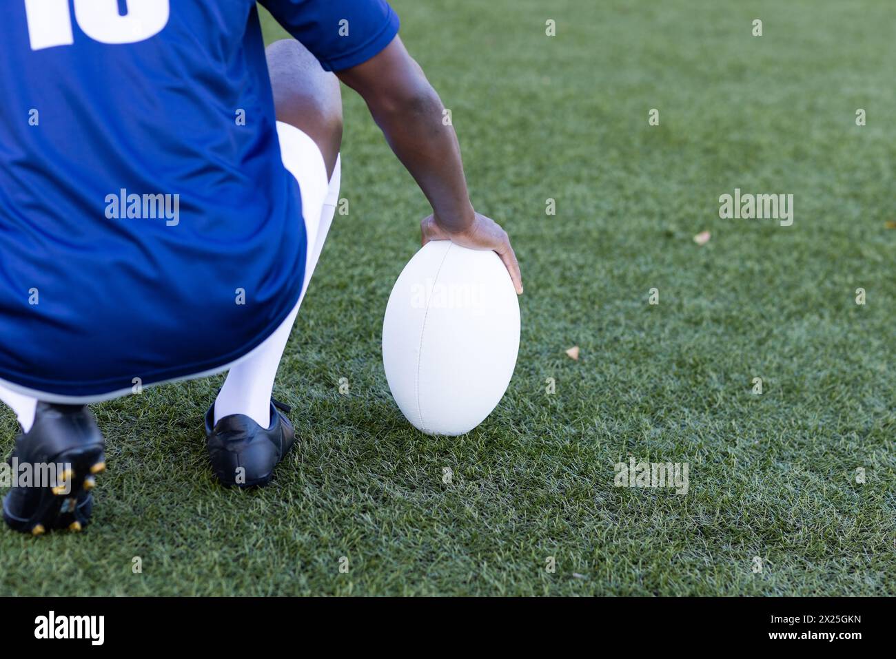 Schwarze Jugendliche in blauem Trikot greifen auf dem Rasenfeld auf Rugby-Ball Stockfoto