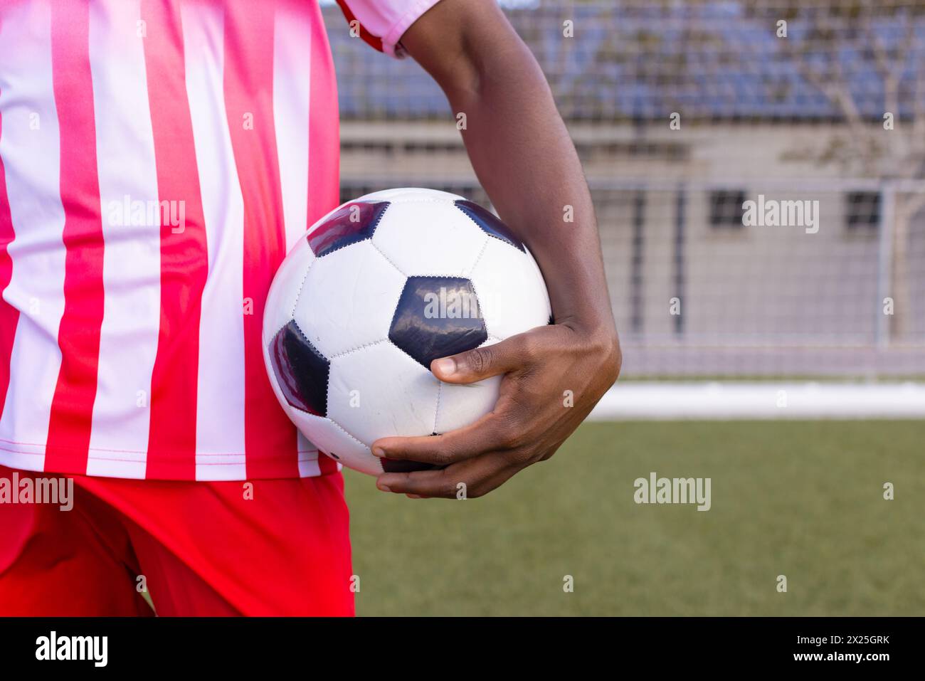 Schwarzer männlicher Athlet in rot-weiß gestreifter Fußballausrüstung hält einen Ball Stockfoto