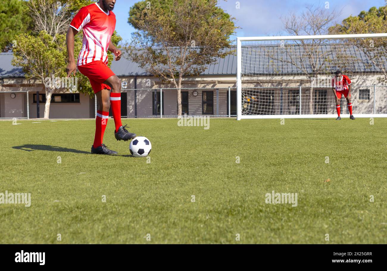 Zwei afroamerikanische Athleten, einer steht kurz vor dem Kicken, spielen im Freien Fußball Stockfoto