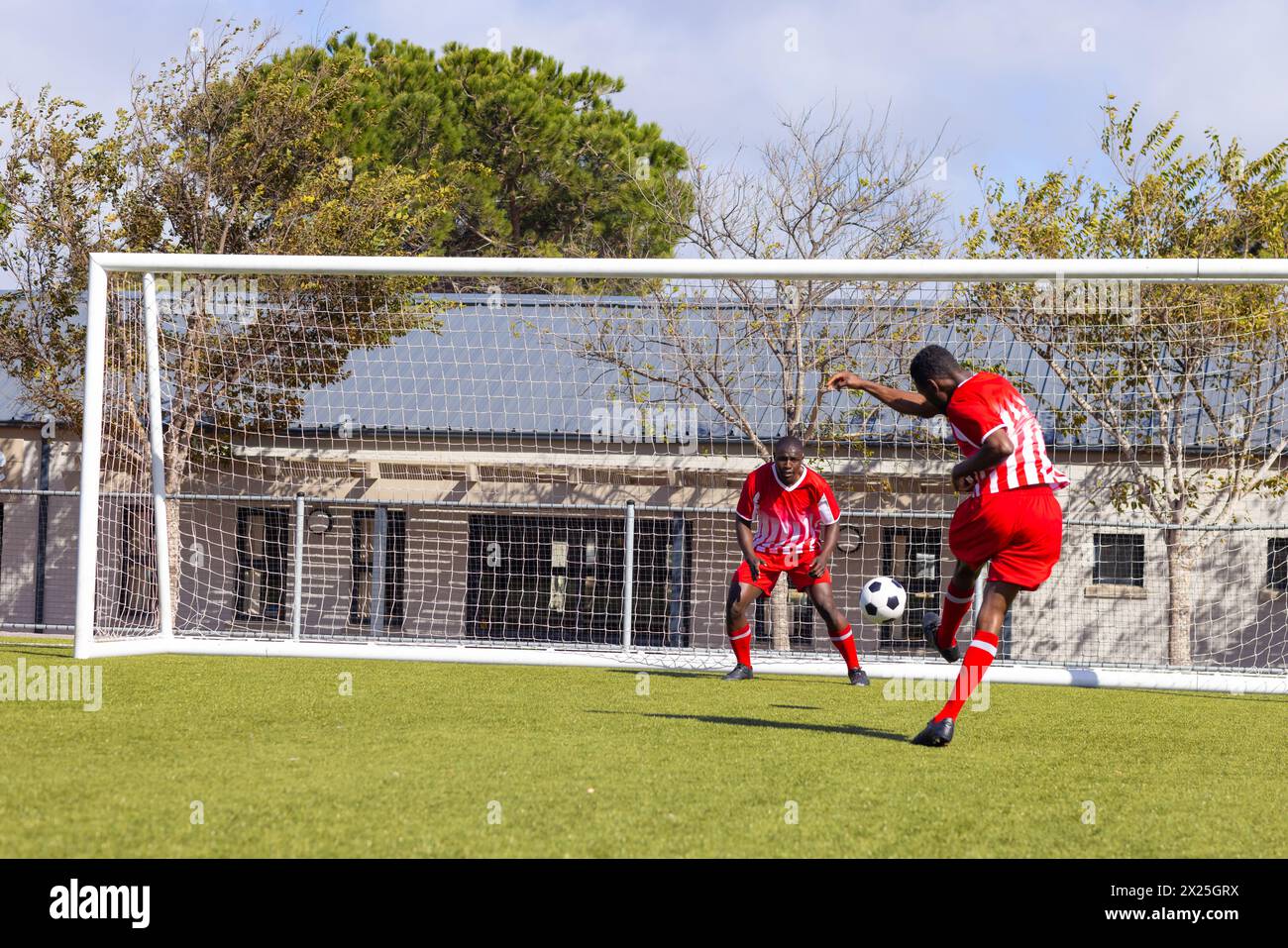 Zwei afroamerikanische junge männliche Athleten spielen auf dem Feld draußen Fußball, einer tritt den Ball Stockfoto