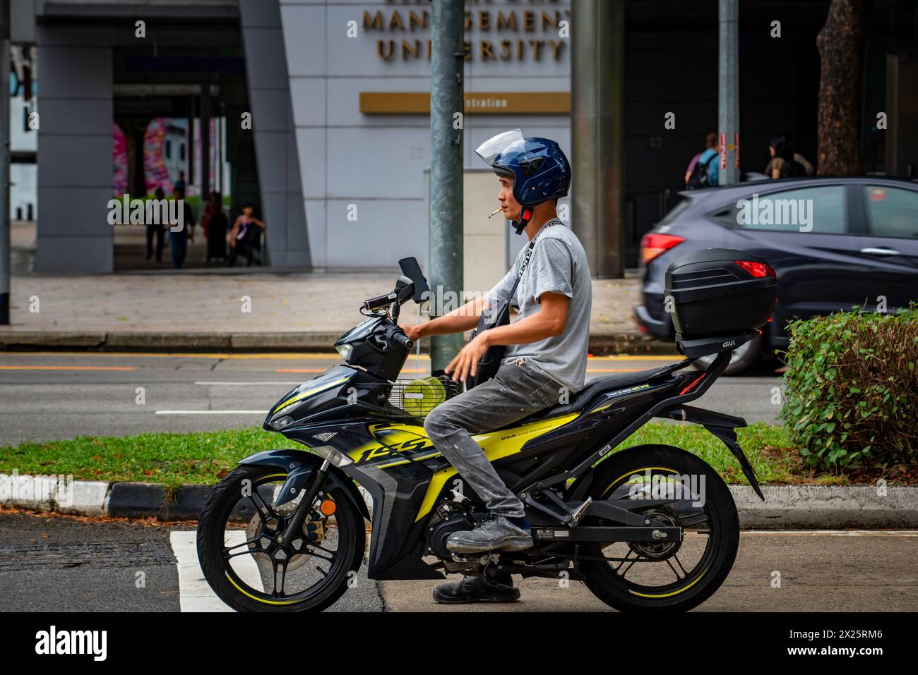 Ein Mann mittleren Alters hielt an der Ampel eines Motorrads oder Motorrollers an und rauchte eine Zigarette in Singapur Stockfoto