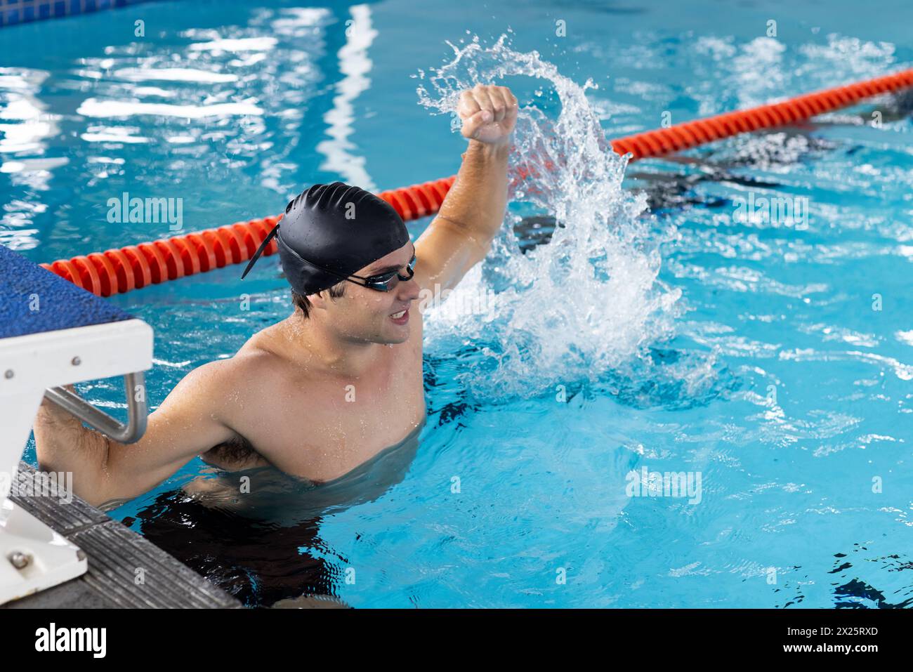 Kaukasischer junger männlicher Schwimmer, der drinnen im Pool feiert und Wasser spritzt Stockfoto
