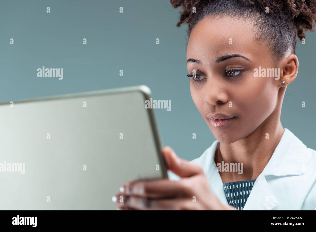 Eine engagierte junge Frau in einem Labormantel taucht in die Forschung auf ihrem Handgerät ein Stockfoto