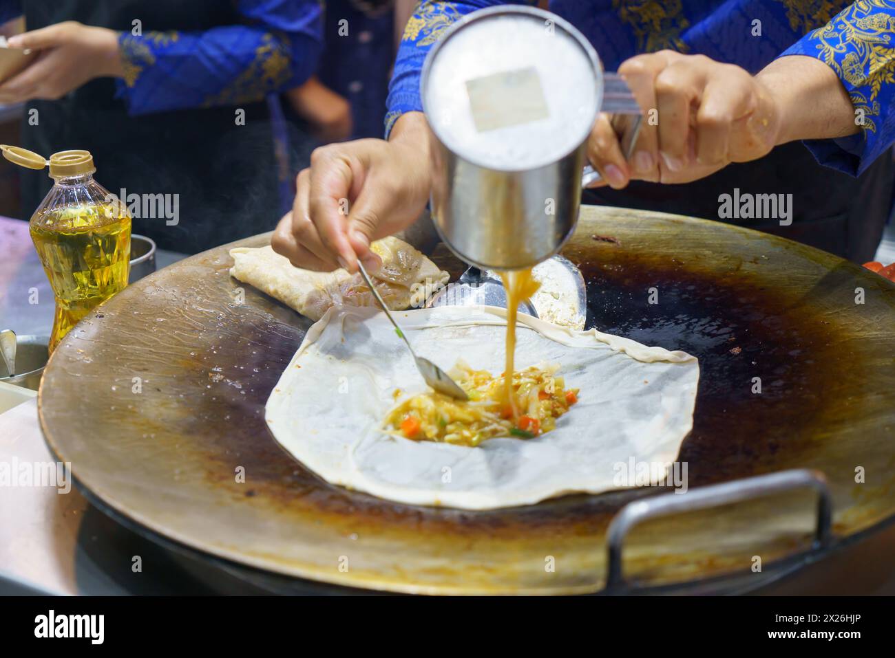 Tauchen Sie ein in die belebten Straßen Thailands mit dieser lebendigen Szene. Ein erfahrener Verkäufer bereitet auf fachmännische Weise knusprige Roti zu, ein beliebtes Street Food de Stockfoto