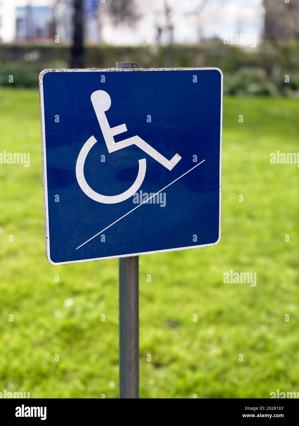 Ein kleines blaues Schild für Rollstuhlbehinderungen steht vor einem verschwommenen Gartenhintergrund und symbolisiert Zugänglichkeit und Inklusivität in Außenbereichen. Stockfoto