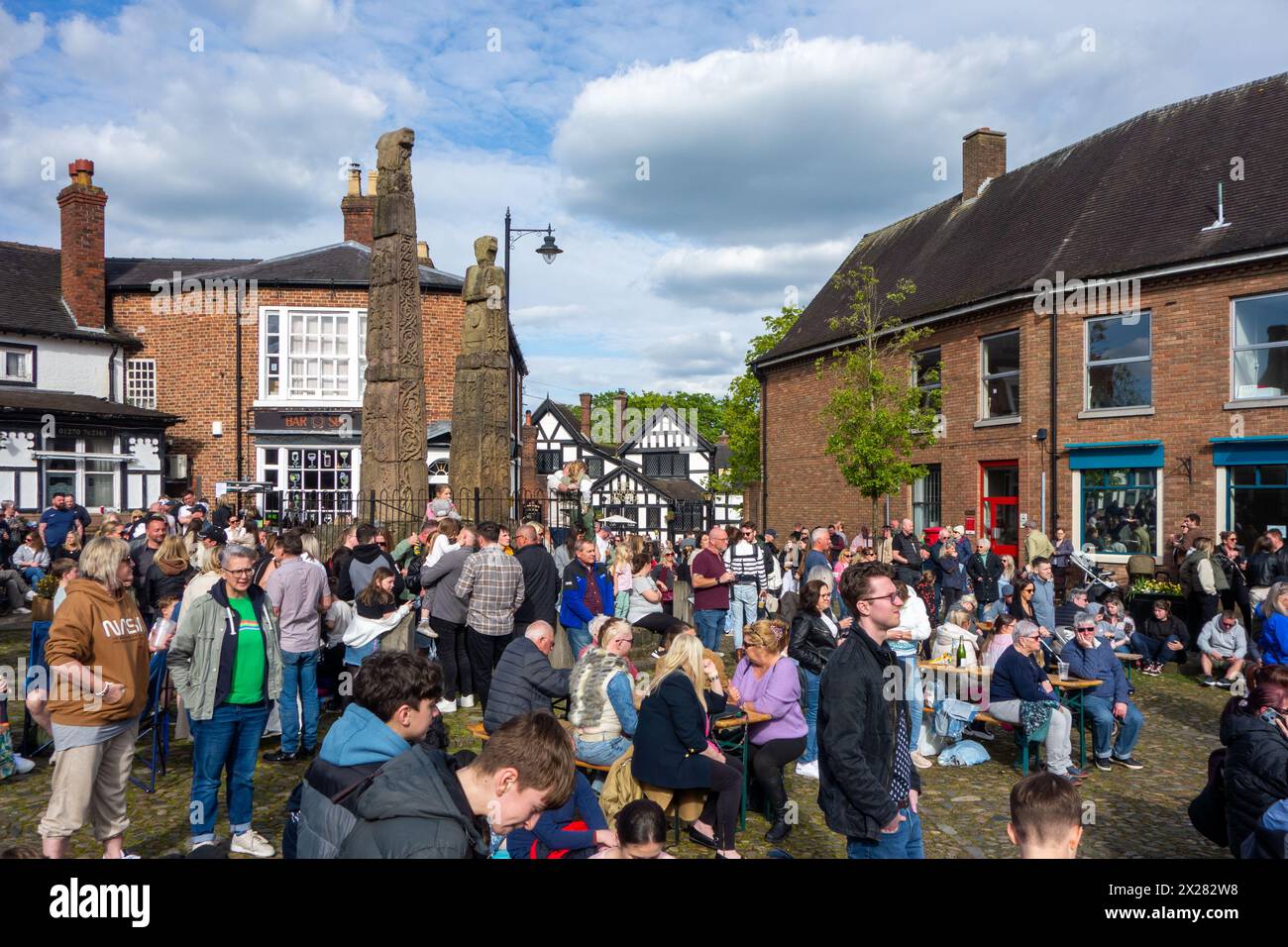 Auf dem mit Kopfsteinpflaster gepflasterten Marktplatz der Marktgemeinde Sandbach in Cheshire können sich Besucher und Festivalbesucher bei einem Musikfestival in der Frühlingssonne erfreuen Stockfoto