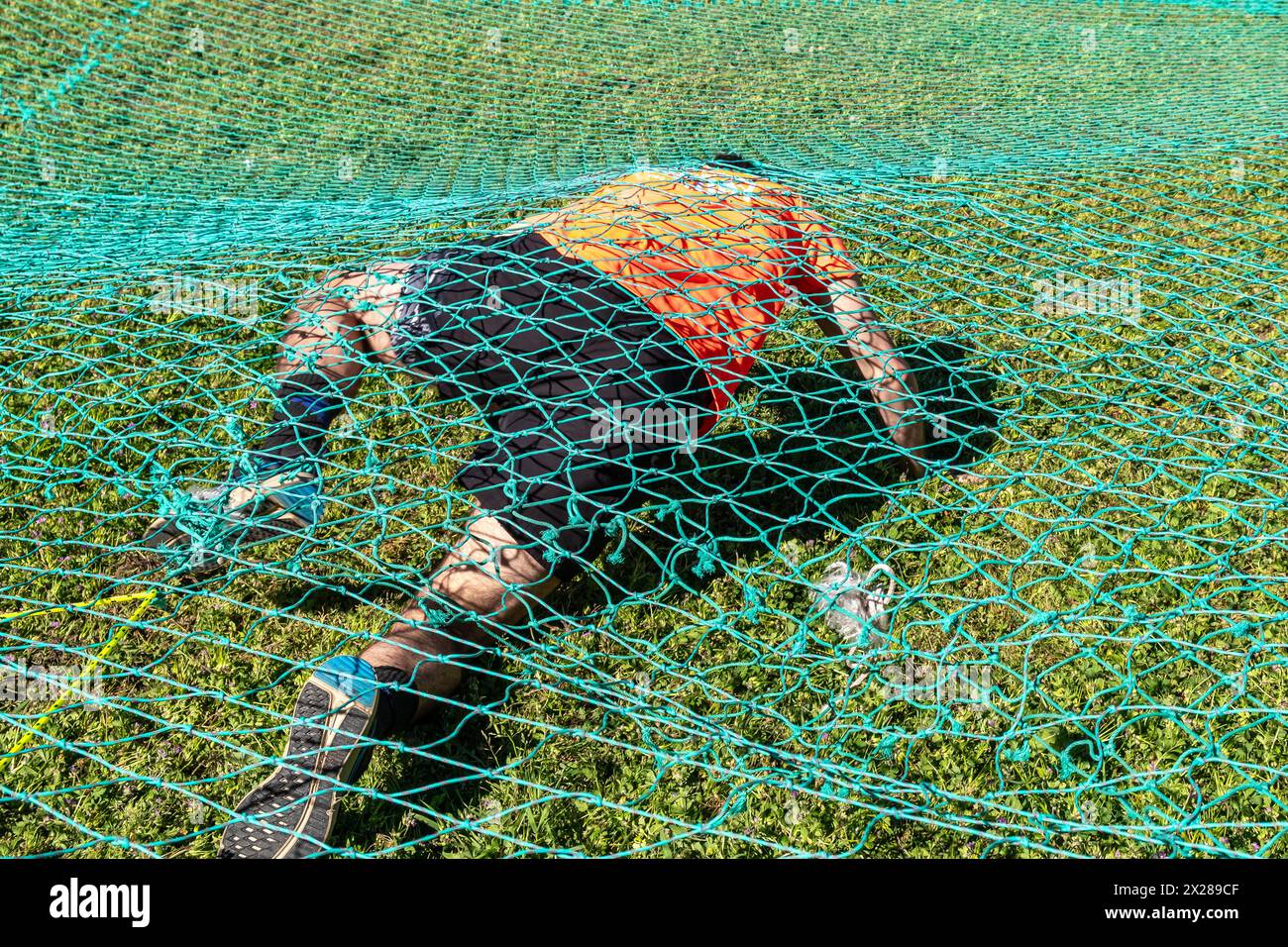 Ein Athlet, der bei einem Hindernisrennen unter einem Netz krabbelt Stockfoto