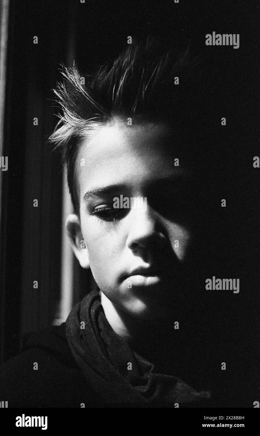 Kopf und Schultern Porträt eines kontemplativen Teenager, der nach unten blickt, Gesicht teilweise im Schatten Stockfoto