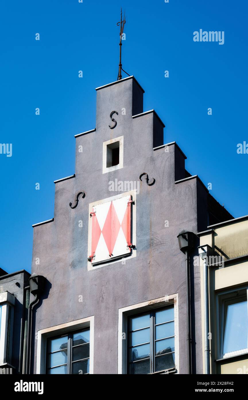 Kleines, schmales, stufenförmiges Giebelhaus mit Wetterfahne und weiß-roten Rollläden in der kölner Altstadt Stockfoto