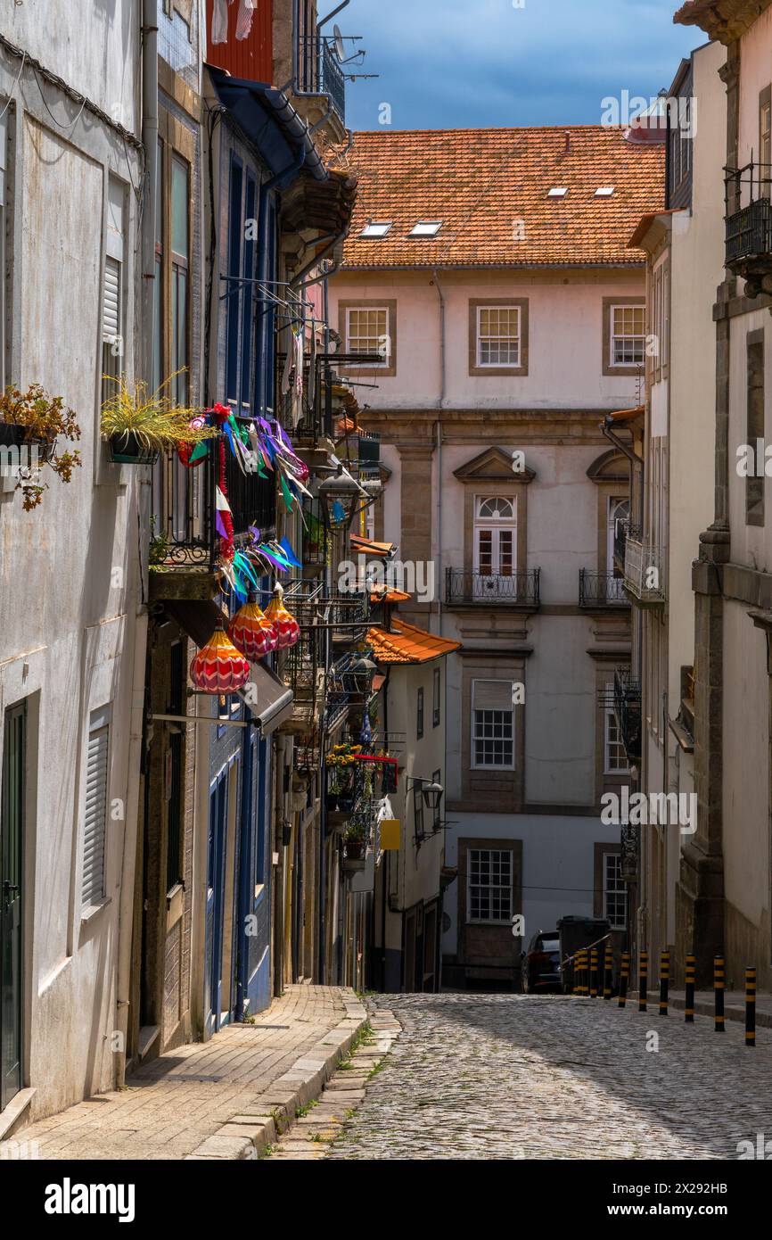Steile, mit Kopfsteinpflaster bewachsene Straße mit Balkonen alter Häuser in einem klassischen und alten Viertel von Porto, dekoriert mit farbigen Papierfahnen und Lant Stockfoto