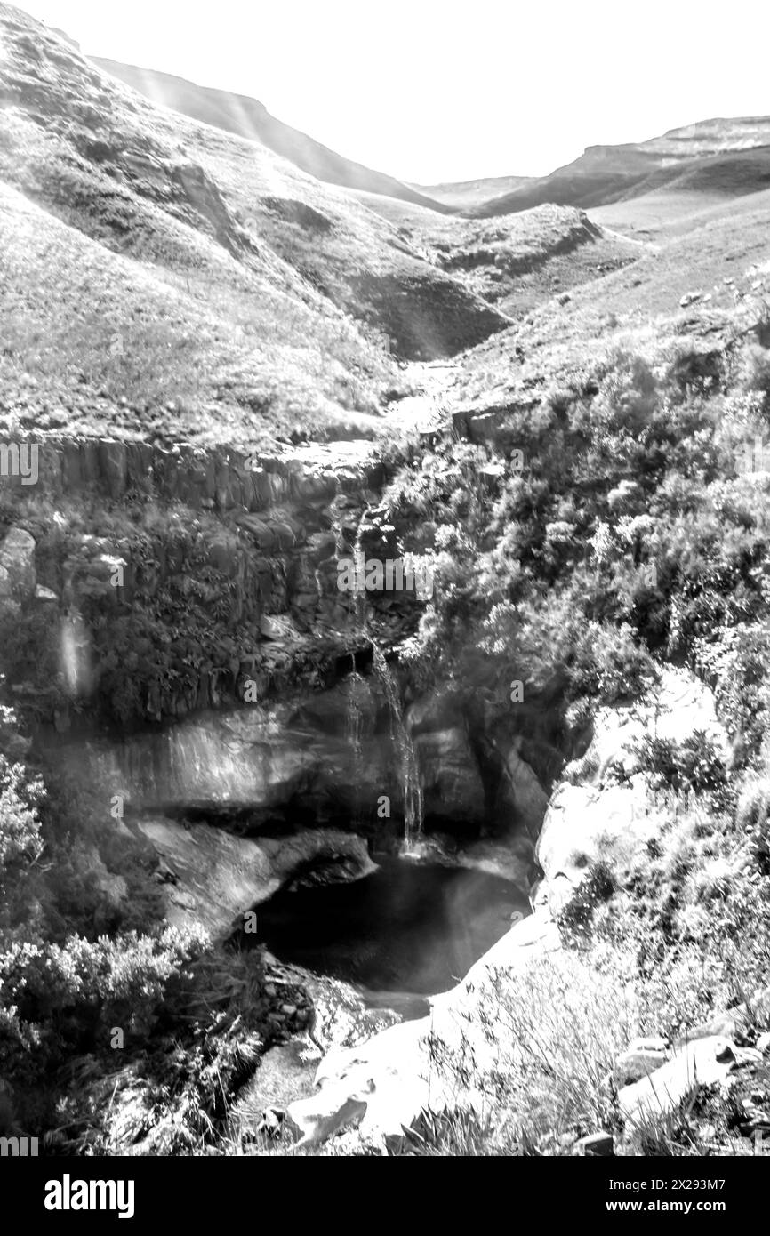 Ein kleiner Wasserfall stürzt in einen tiefen, abgeschiedenen Pool in den Drakensberg Mountains des Golden Gate National Park Südafrika in Schwarz-weiß Stockfoto
