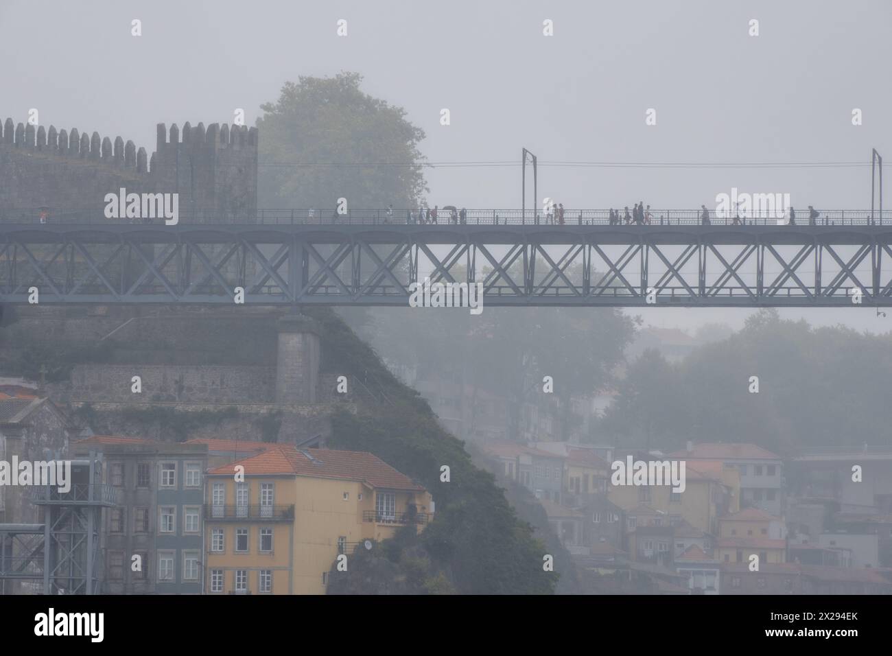 Menschen mit Regenschirmen und Regenmänteln gehen auf der oberen Plattform der Stahlbrücke Don Luis I mit der mittelalterlichen Mauer darunter, der Standseilbahn und dem o Stockfoto