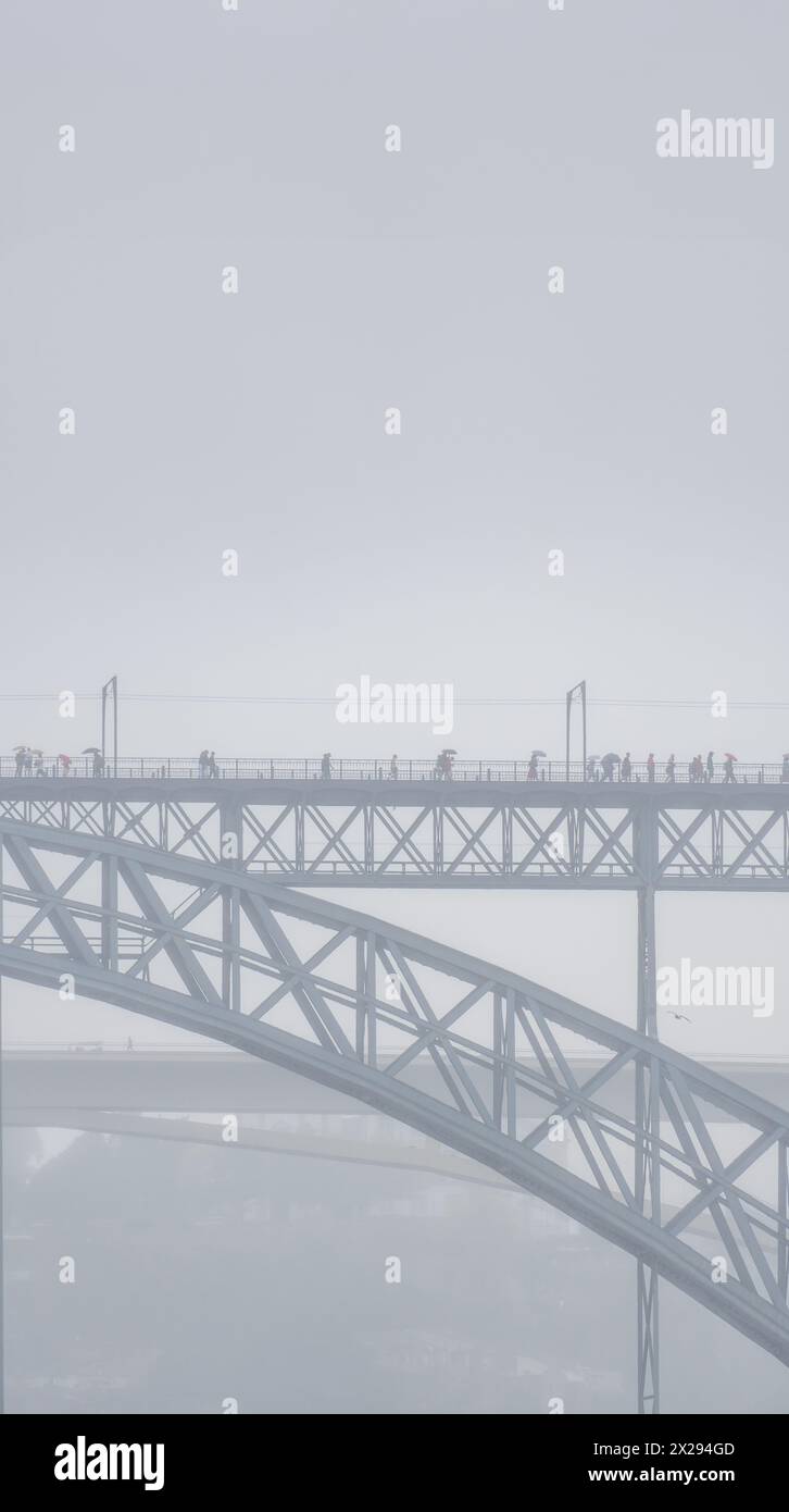 Menschen mit Regenschirmen und Regenmänteln gehen auf der oberen Plattform der Don Luis I Stahlbrücke und Autos fahren auf der unteren Plattform mit einer Person Stockfoto