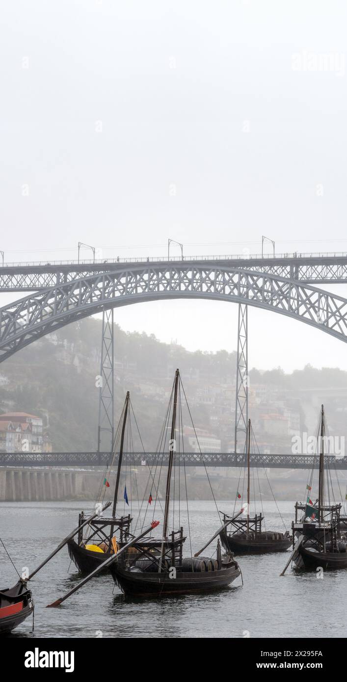 Klassische Holzboote mit Weinfässern, die am Fluss Douro in Porto unter der Stahlbrücke Don Luis I im Hintergrund angedockt sind Stockfoto