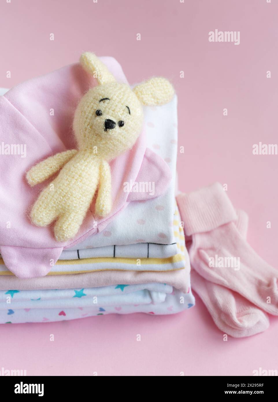 Ein Stapel Babybody. Baby-Strickspielzeug aus Häschen neben einem Stack-Strampler für Kinder Stockfoto