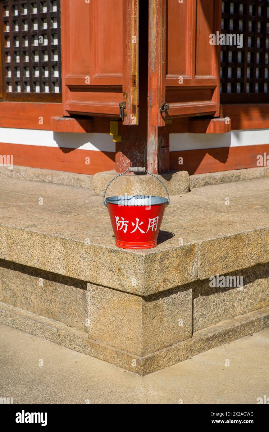 Ein roter Eimer mit der japanischen Aufschrift „for Fire Protection“ vor einem alten Holzgebäude Stockfoto