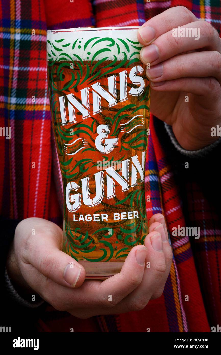 Eine Hand hält ein Pint Innis and Gunn Lager in einem Markenglas vor einem Tartan-Hintergrund, Schottland, UK Stockfoto