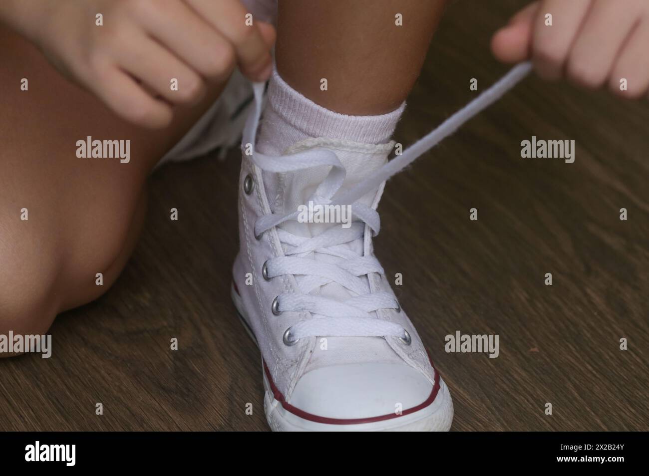Kinder binden Schuhe. Ein kleines Mädchen, das Probleme hat, Schuhschnürsenkel zu binden. Das Kind lernt feinmotorische Fähigkeiten. Stockfoto