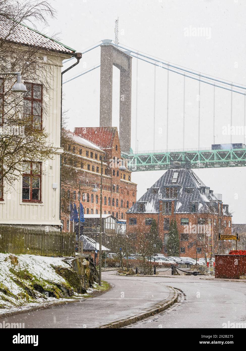 In Göteborg entfaltet sich eine ruhige Winterszene, während der sanfte Schneefall die Straßen der Stadt bedeckt und die beeindruckende Struktur einer Hängebrücke hoch aufragt Stockfoto