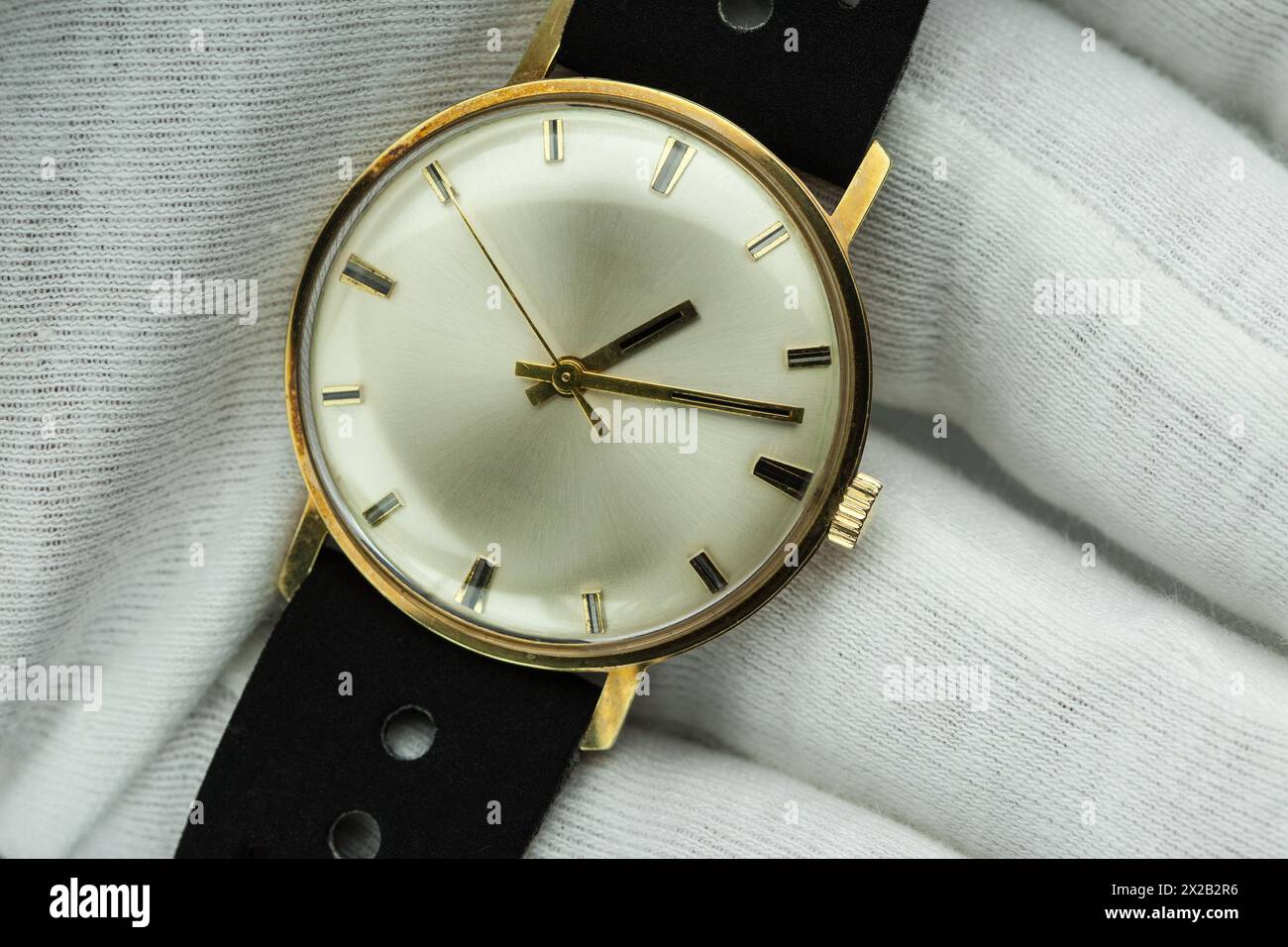 Uhrmacher in weißen Handschuhen präsentiert stolz eine handgefertigte goldene Uhr aus den 1960er Jahren - ein Meisterwerk vergangener Eleganz und Präzision. Stockfoto