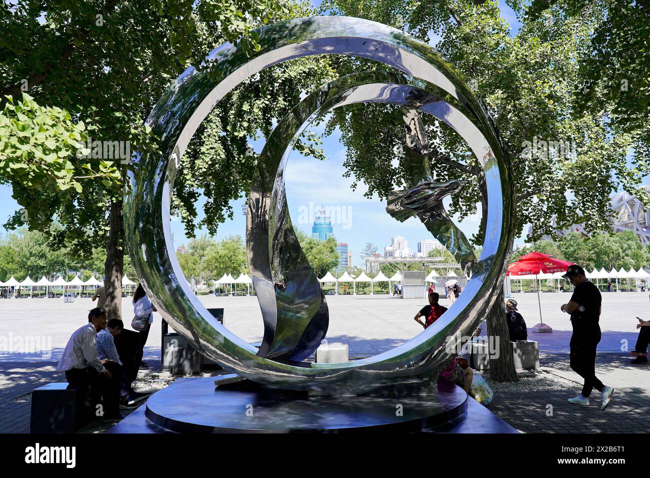 Peking, China, Asien, reflektierende Skulptur im öffentlichen Raum, umgeben von Bäumen und sitzenden Menschen Stockfoto