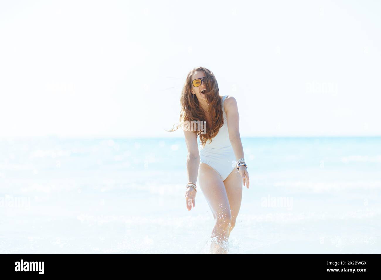 Glückliche, elegante Frau an der Küste, die Spaß im Wasser hat. Stockfoto