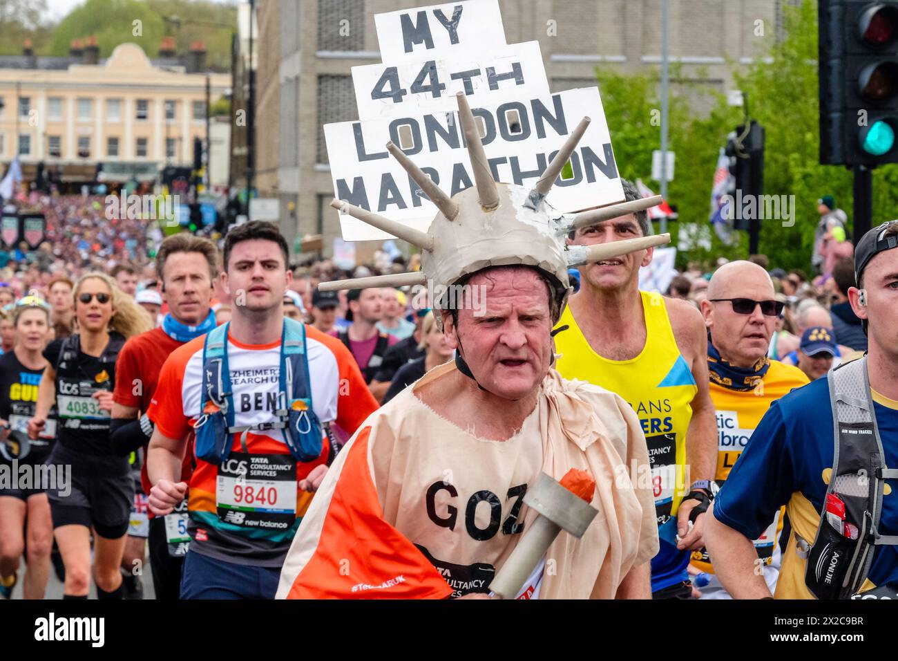 London Marathon 2024: Läufer im Kostüm mit Schild, das ihn zum 44. London Marathon erklärt. Stockfoto