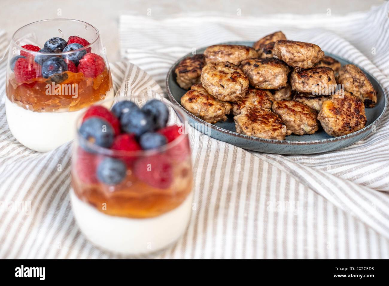 Mehrschichtiges Beerendessert und saftige Fleischbällchen auf einem strukturierten Tuch, schaffen eine heimische Gastronomie-Szene. Hochwertige Fotos Stockfoto
