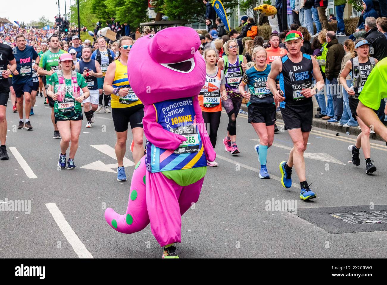 London Marathon 2024: Teilnehmer im pinken Dinosaurierkostüm zur Unterstützung einer Wohltätigkeitsorganisation für Bauchspeicheldrüsenkrebs auf der Route des 44. Londoner Marathons. Stockfoto