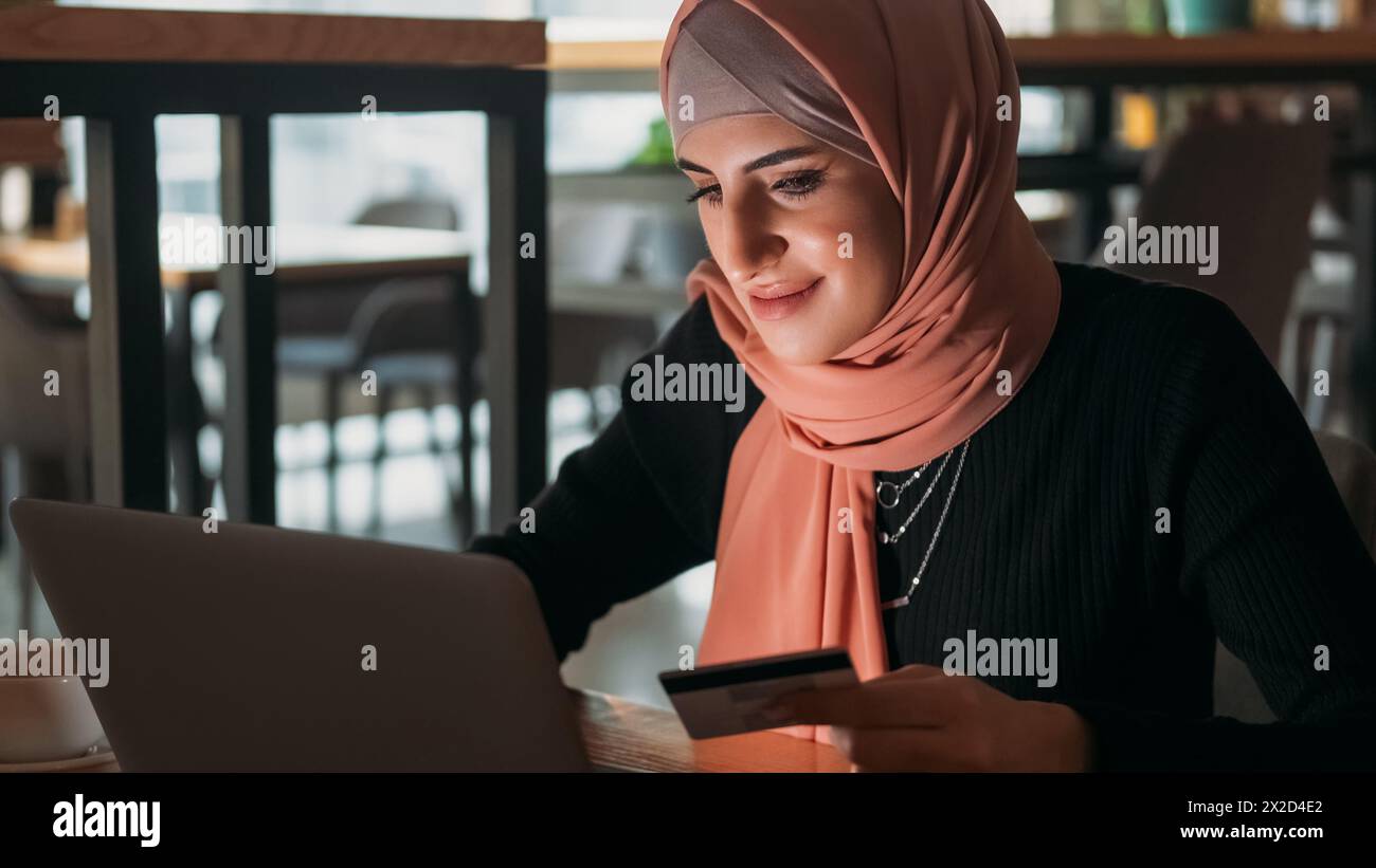 Online-Zahlung. Internet-Kauf. Lächelnde Frau im Hijab, die mit Kreditkarte, E-Commerce-Service, Geldtransfer im Café bestellt. Stockfoto