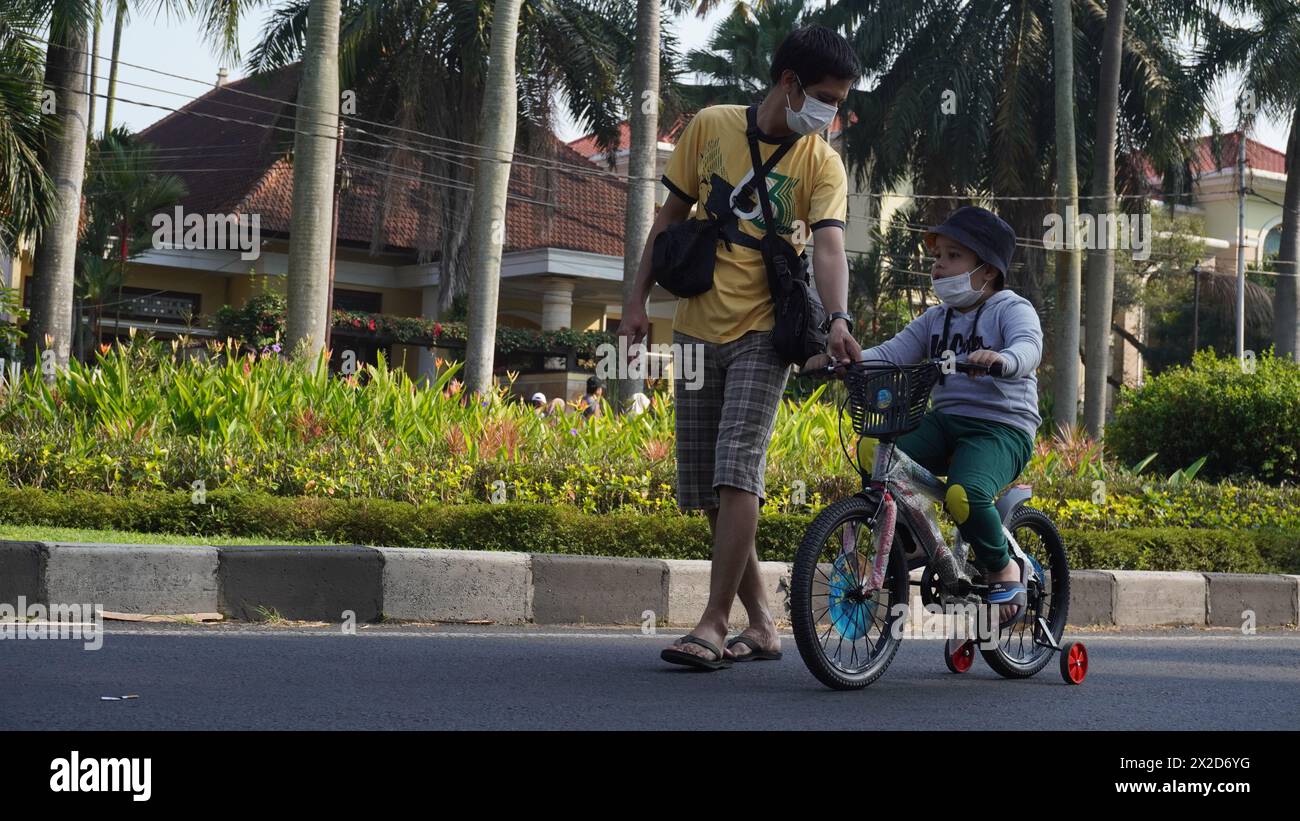 Ein Vater, der spaziert und sich um seinen Sohn kümmert, der in der autofreien Gegend von Malang mit einem Vierrad fährt Stockfoto